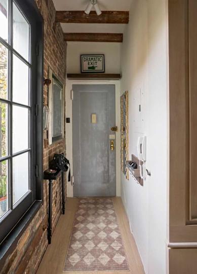 Narrow hallway with exposed brick walls, a gray door, a patterned rug, and a "Dramatic Exit" sign.