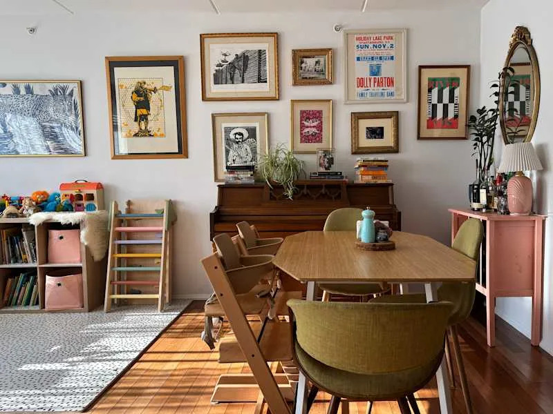 Dining area featuring a wooden table, green chairs, a pink side table, and framed artwork on the walls.