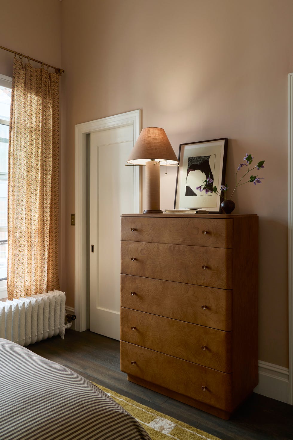 Interior space featuring a wooden dresser with a lamp, framed artwork, and curtains.