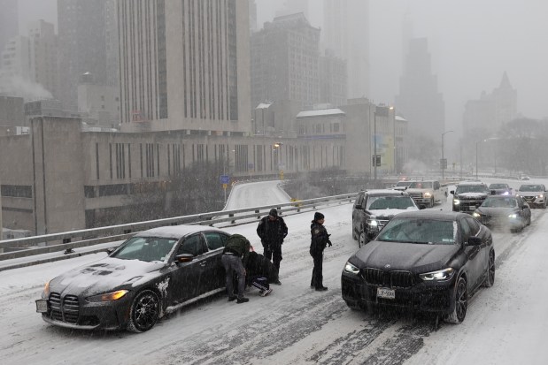 Police direct traffic past a car stuck going across the Brooklyn Bridge as it snows on Sunday, Jan. 25, 2026, in New York. (AP Photo/Alyssa Goodman)