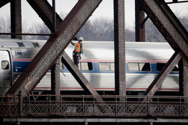 A man works on a rail bridge spanning the Hudson River as an Amtrak passenger train passes on Friday, Dec. 18, 2015, in Albany, N.Y. (AP Photo/Mike Groll)
