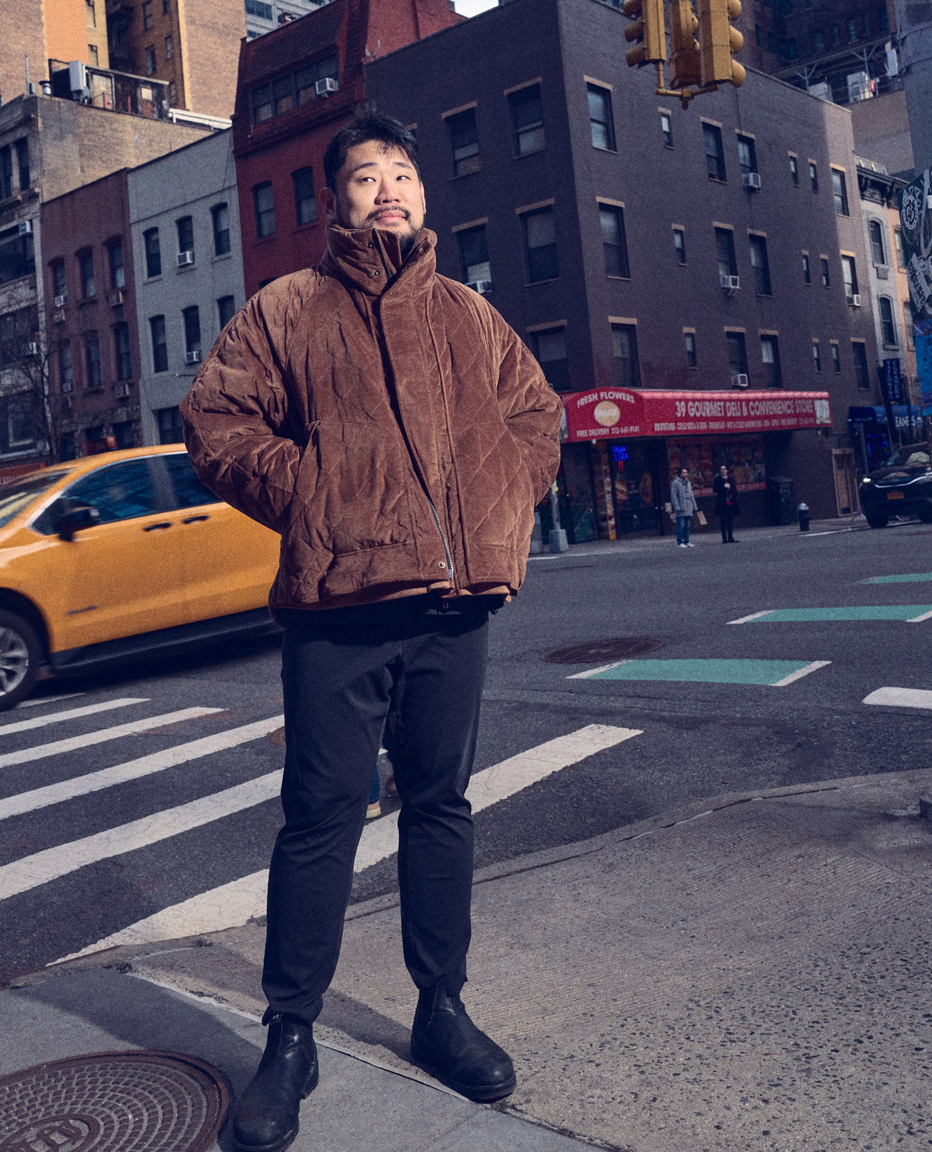 A man in a brown coat and black pants standing outside in a city.