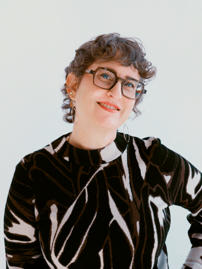 Person with short curly hair and glasses, wearing a patterned sweater.