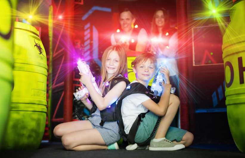 Happy little brother and sister sitting back to back in colorful laser beams holding laser guns during lasertag game with family in labyrinth laser tag nyc