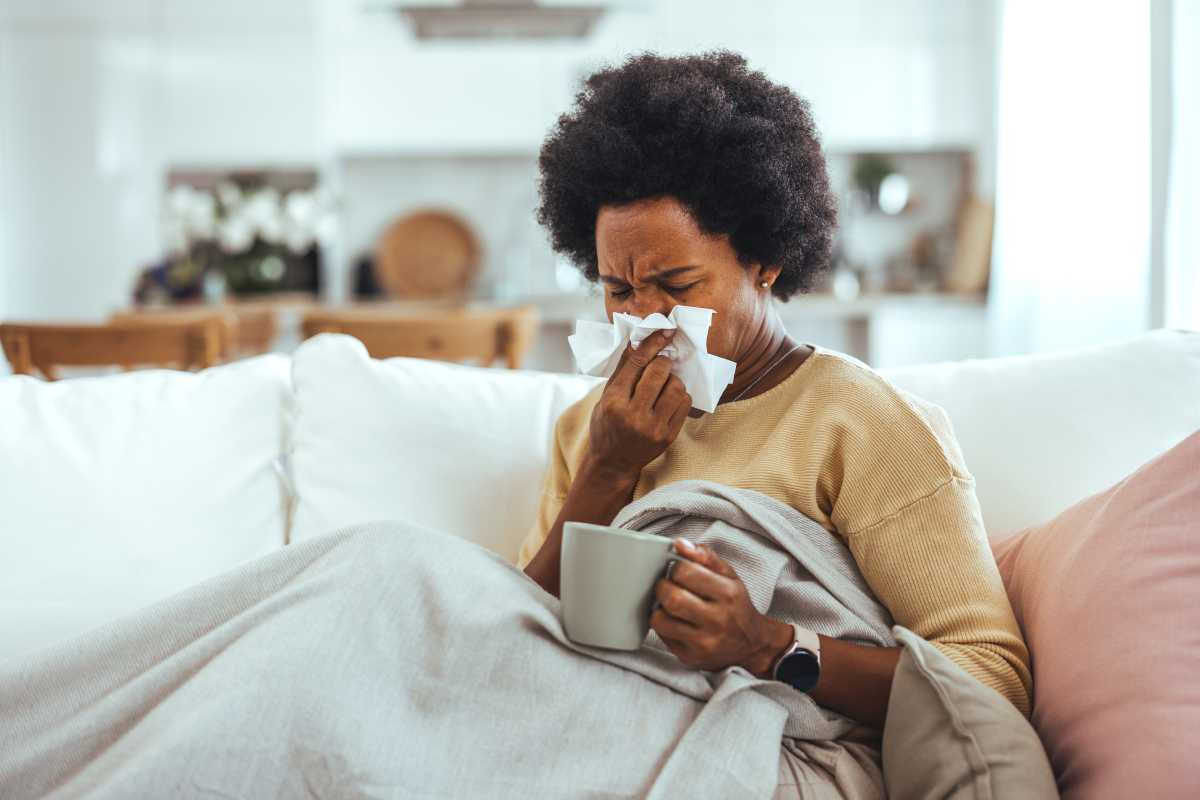 woman sneezing on couch amid spike in flu cases