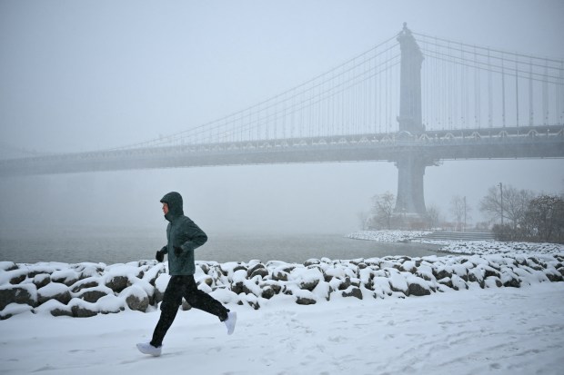 A man runs in the snow near the Manhattan Bridge in the Brooklyn Borough of New York City on January 25, 2026. A massive winter storm on January 24 dumped snow and freezing rain from New Mexico to North Carolina as it swept across the United States towards the northeast, threatening tens of millions of Americans with blackouts, transportation chaos and bone-chilling cold. After battering the country's southwest and central areas, the storm system began to hit the heavily populated mid-Atlantic and northeastern states as a frigid air mass settled in across the nation. (Photo by ANGELA WEISS / AFP via Getty Images)