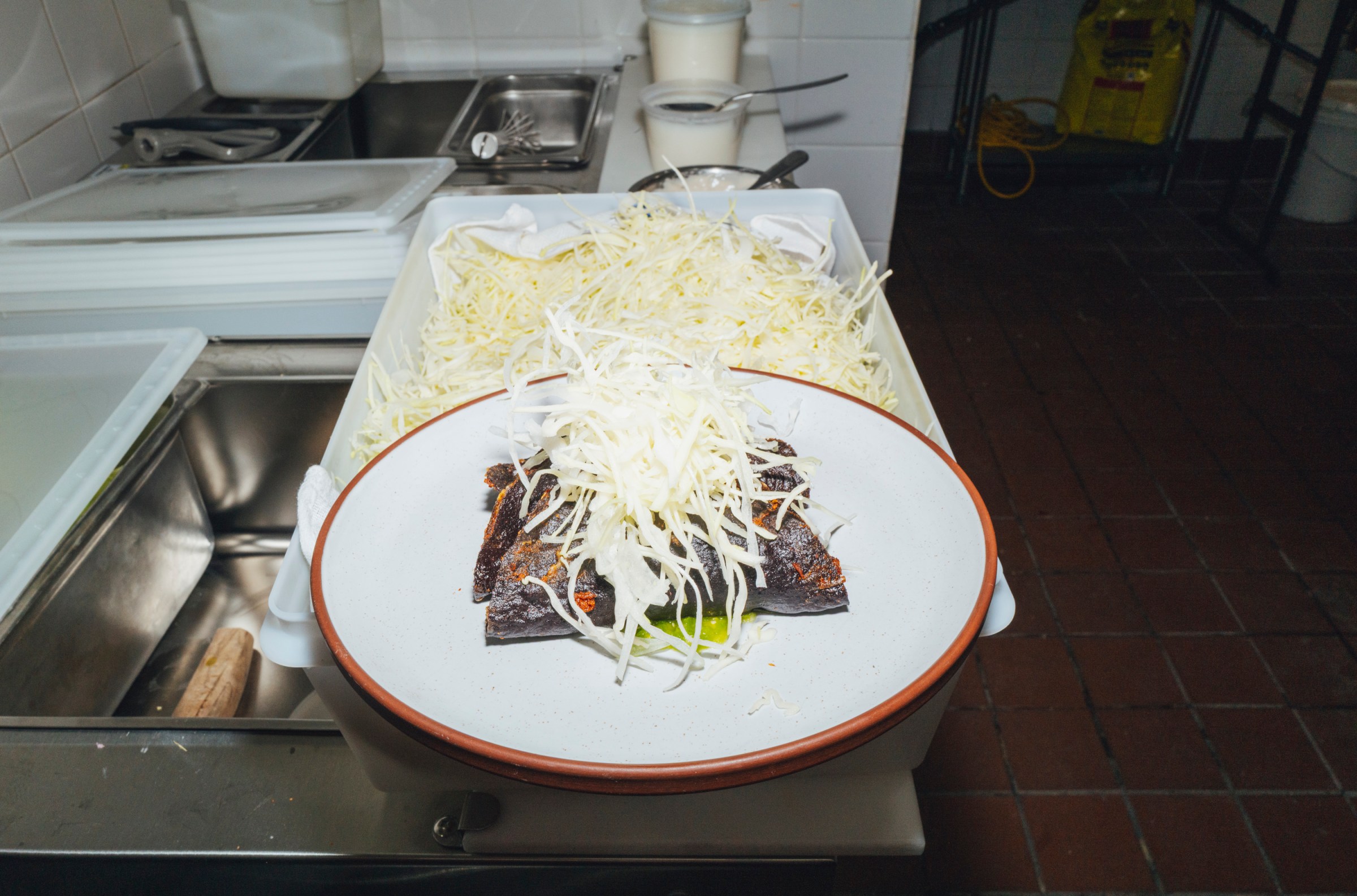 A plate of dark tacos with a pile of shredded cheese on top of it.
