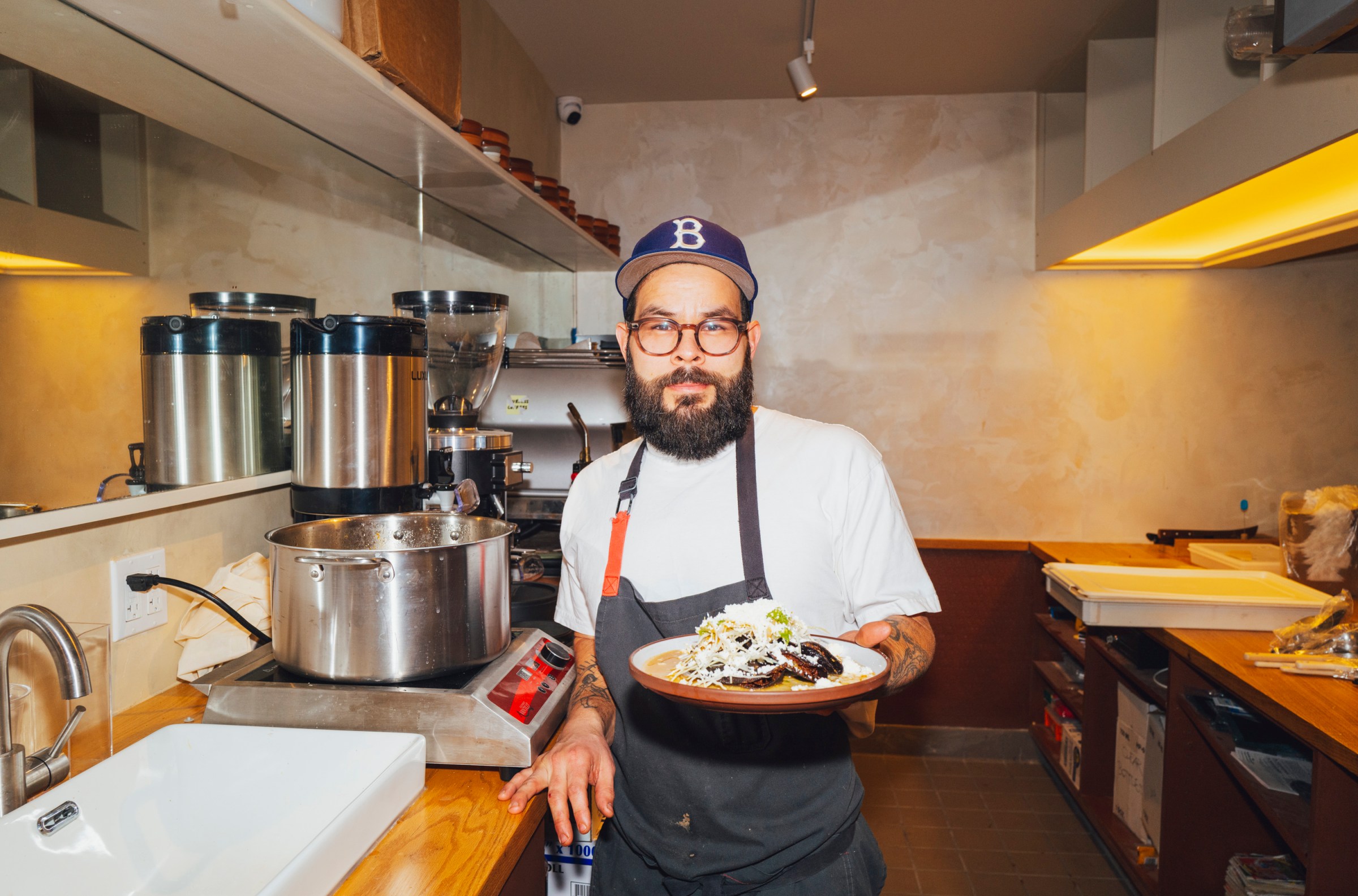 A person in a kitchen holding up a plate of tacos.
