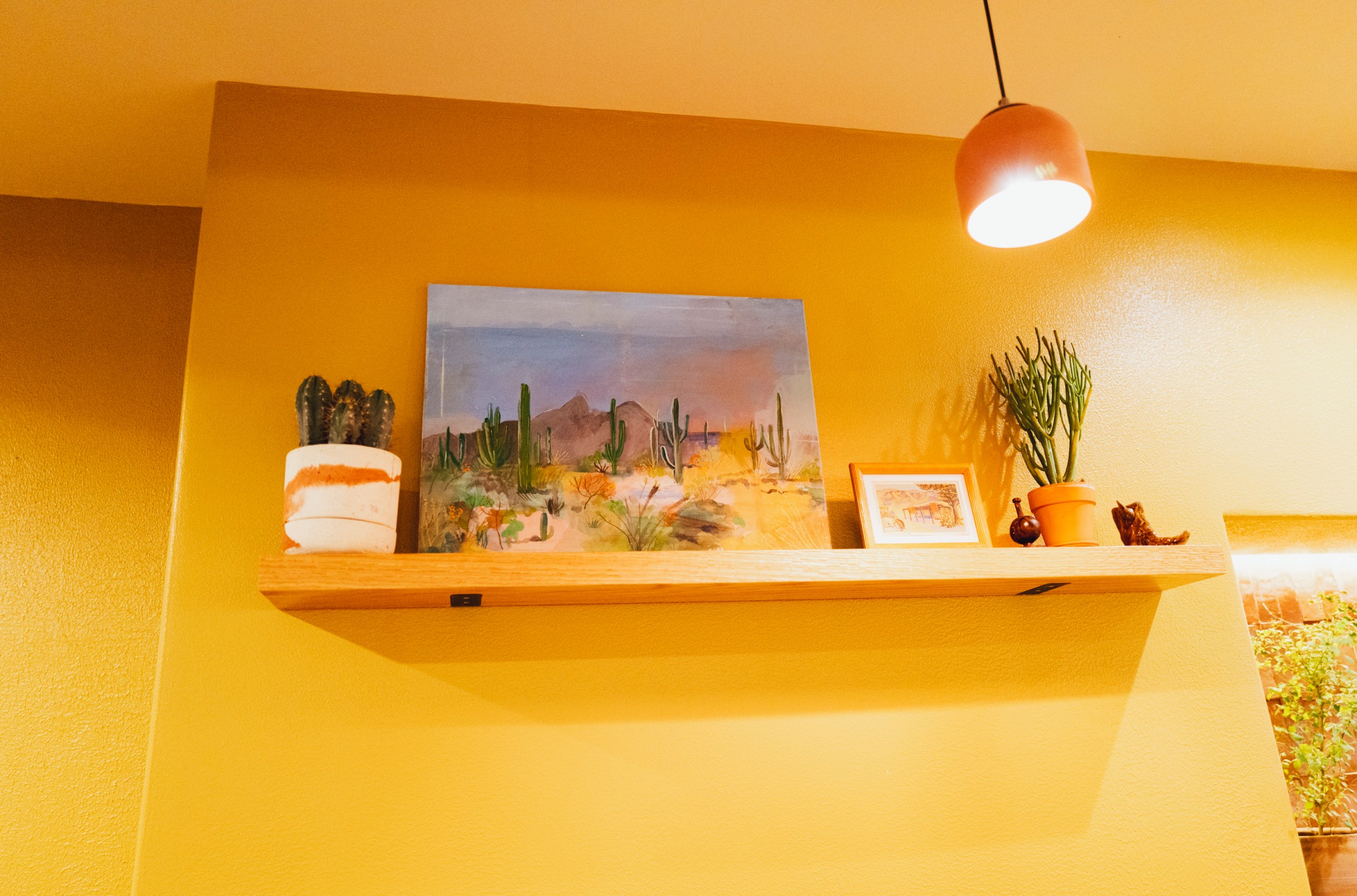 A floating shelf with a painting and some plants.