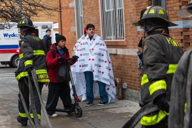 Displaced residents wait on the sidewalk after a five-alarm fire destroyed a row of apartment buildings on Madison St. near Onderdonk Ave. in Ridgewood, Queens, on Tuesday, Jan. 6, 2025. (Gardiner Anderson / New York Daily News)