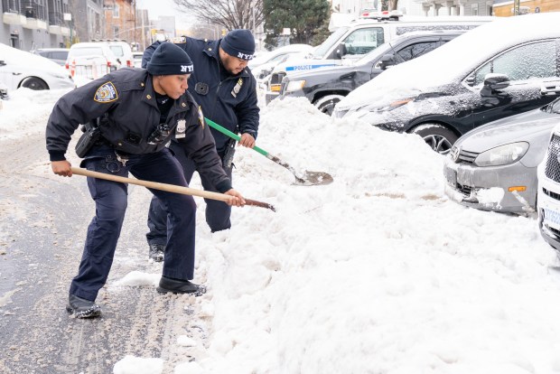 NYPD officers clear snow outside of the 67th Precinct station house in Brooklyn on Monday morning.