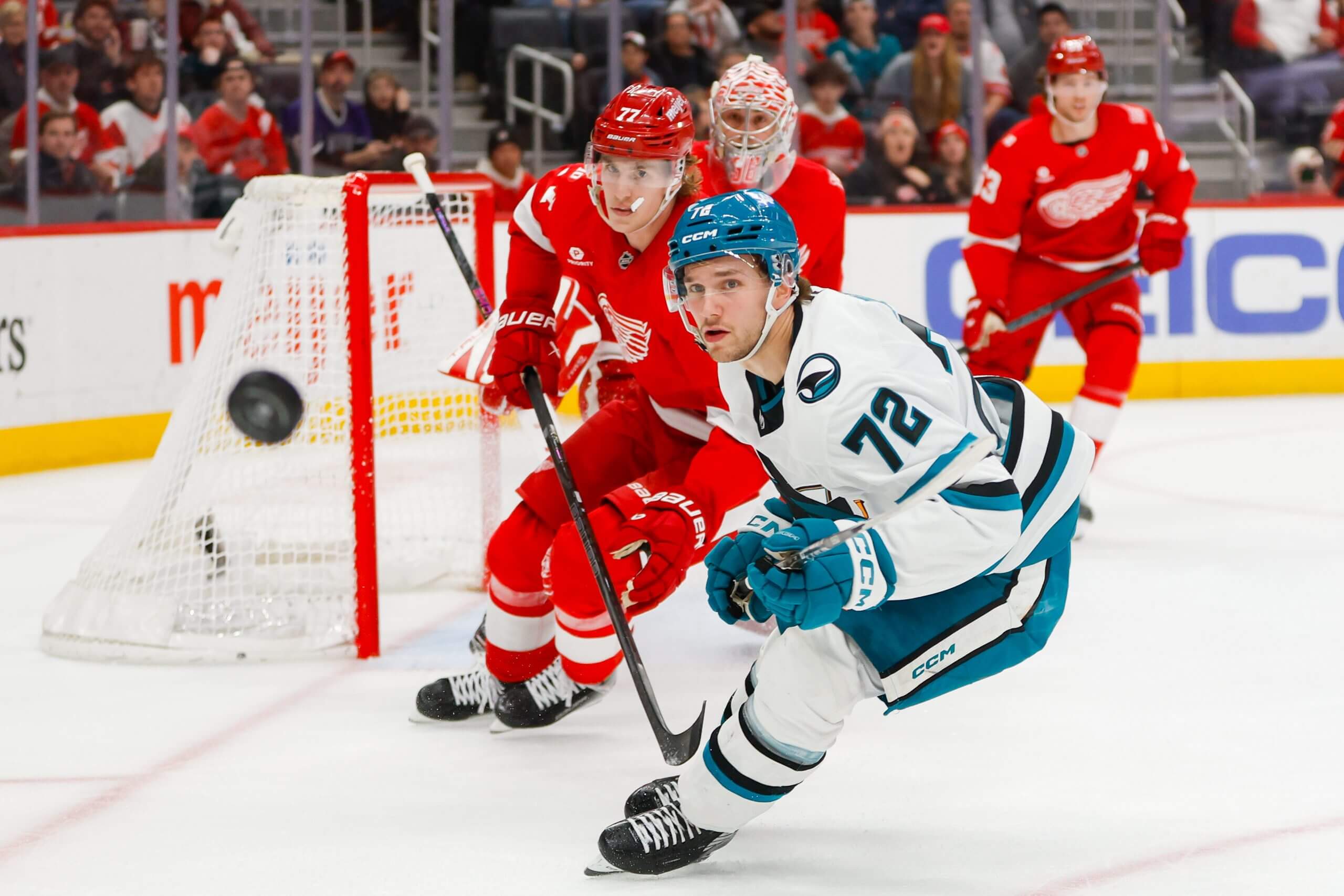 William Eklund watches a flying puck pursued by a Red Wings defenseman.
