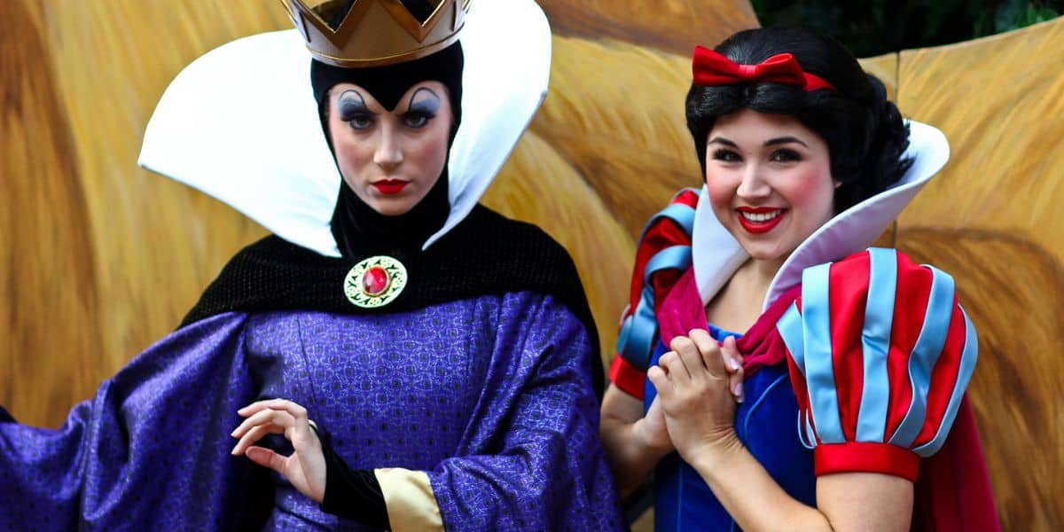 The Evil Queen and Snow White greet guests in vibrant costumes, the Queen regal and serious while Snow White beams with a warm smile.