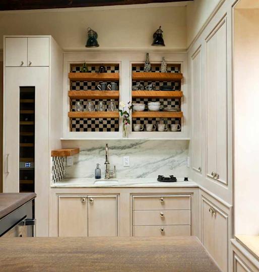 Modern kitchen with light wood cabinetry, open shelving displaying glassware and ceramics, marble countertop, and a sink.