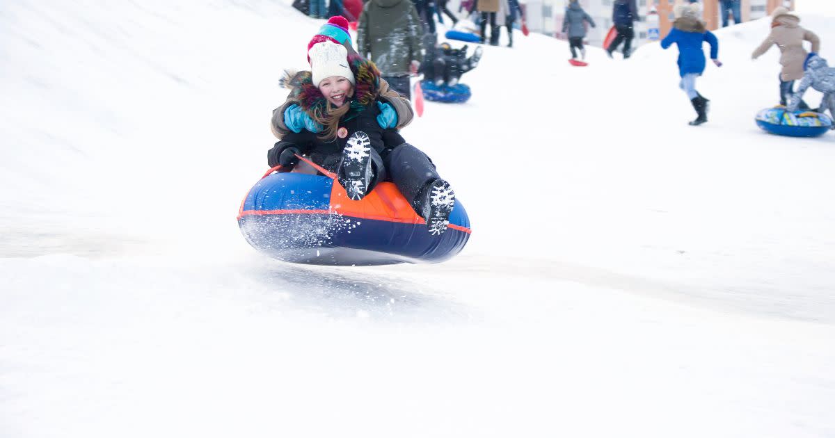 A tween girl is happily sledding down a snowy hill in Central Park on a tube.
