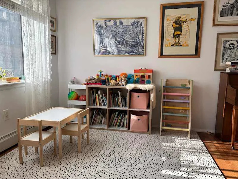 Bright playroom with a small wooden table and chairs, colorful toys, bookshelves, and playful decor.