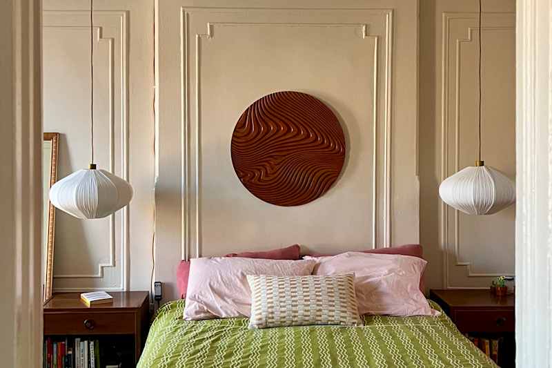 Cozy bedroom featuring a green bedspread, pink pillows, a decorative wall art piece, and pendant lights.