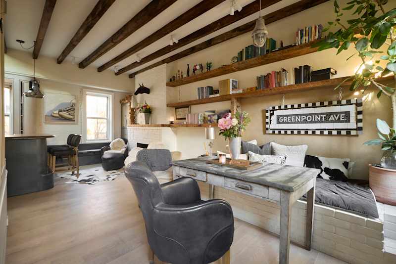 Cozy living space with exposed wooden beams, a rustic desk, bookshelves, and a decorative sign.