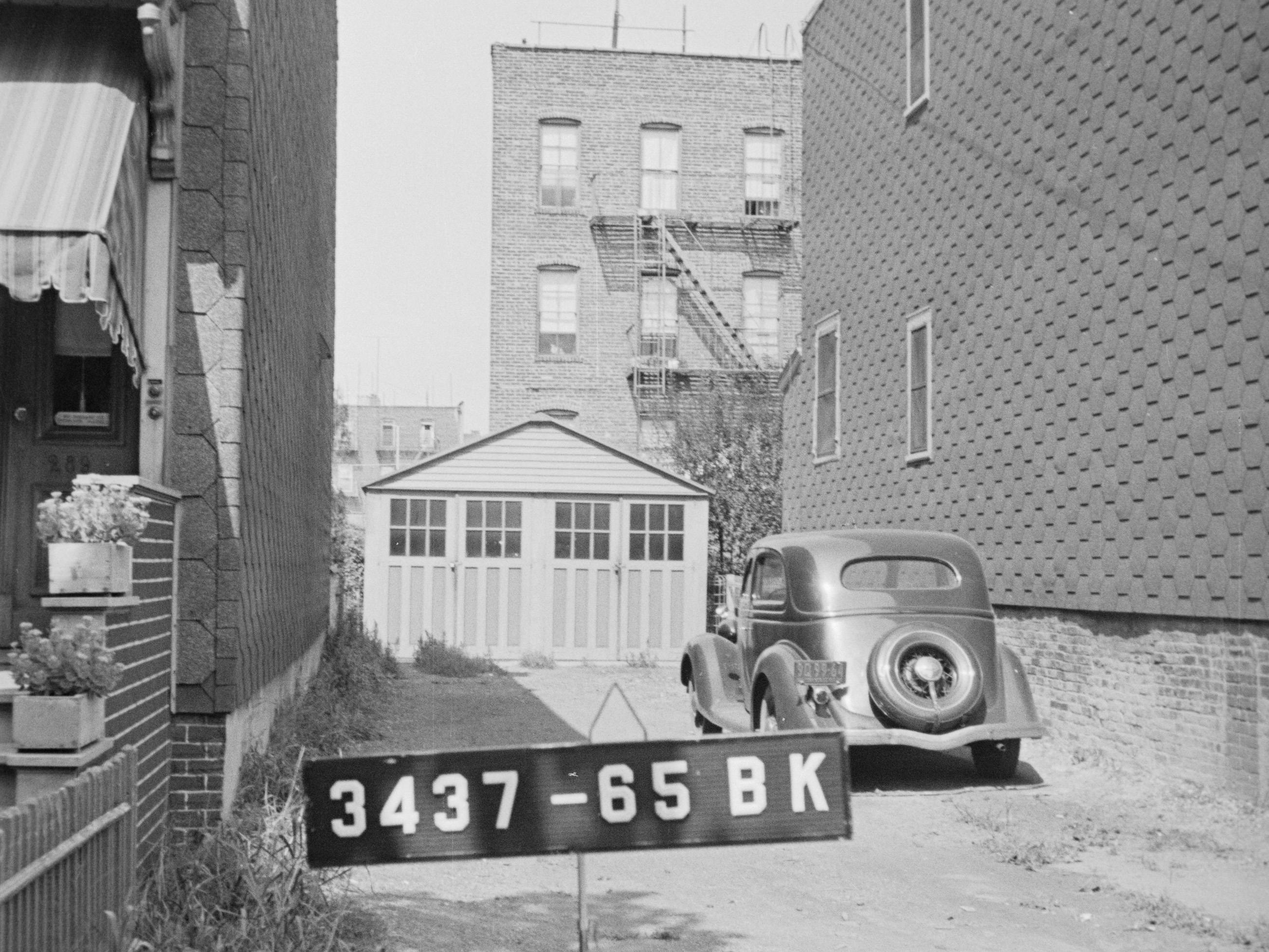 black and white photo of a car in front of a garage
