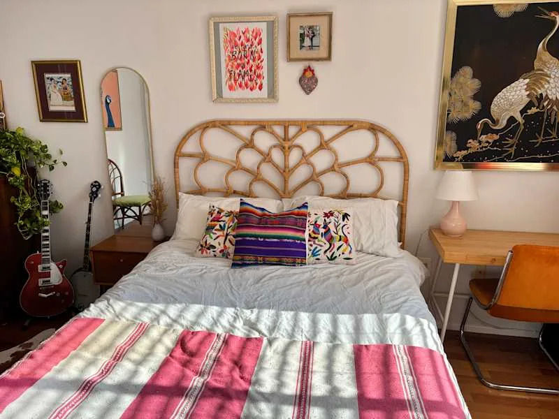 Cozy bedroom featuring a rattan headboard, colorful pillows, a guitar, and a wooden desk with an orange chair.