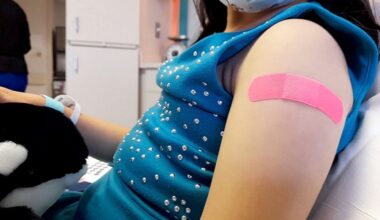 child shows bandage on her left arm after receiving vaccine