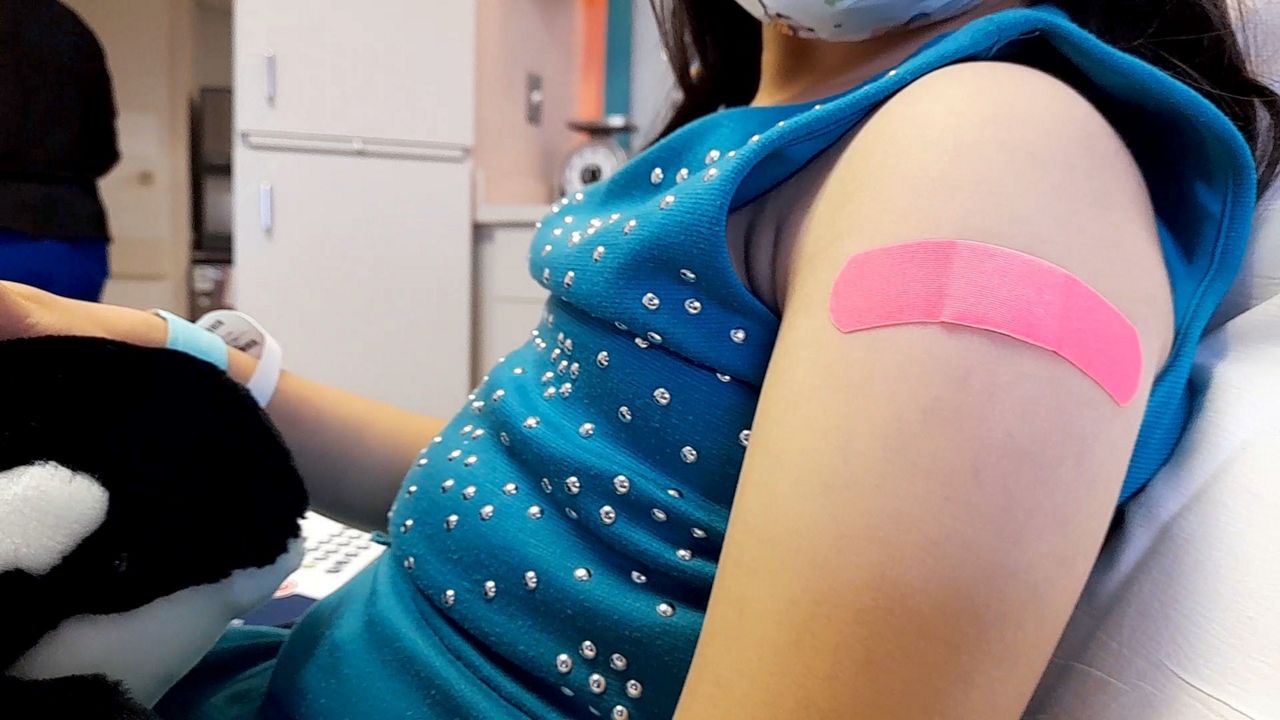 child shows bandage on her left arm after receiving vaccine
