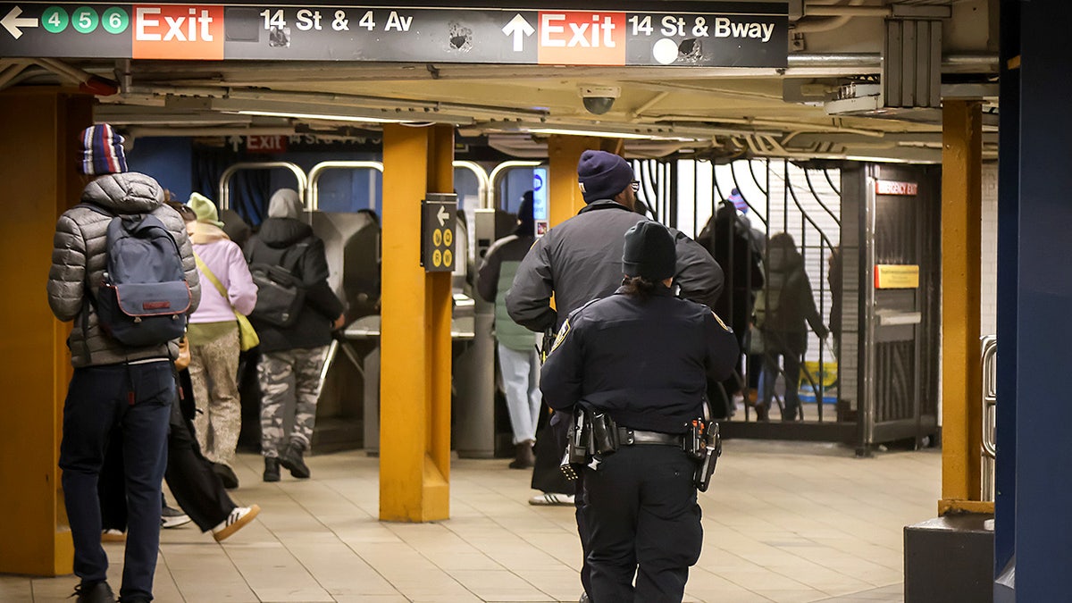 New York Police Department officers stand inside a subway station near turnstiles and platforms.