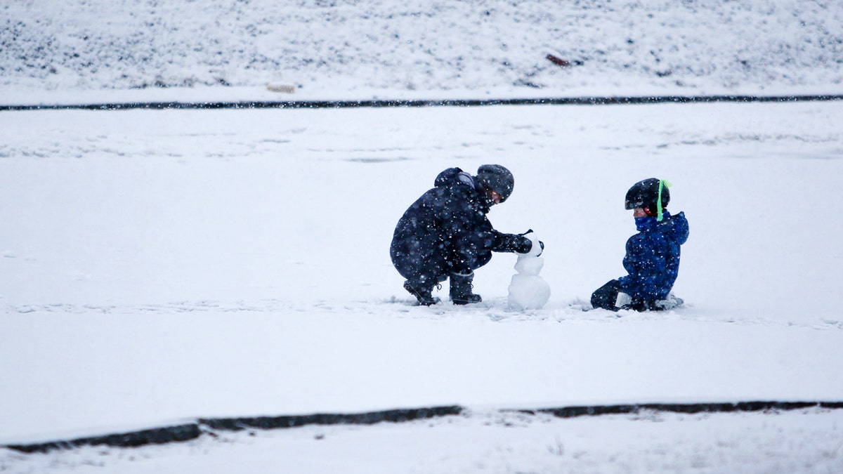 woman and child outside in snow, building a snowman
