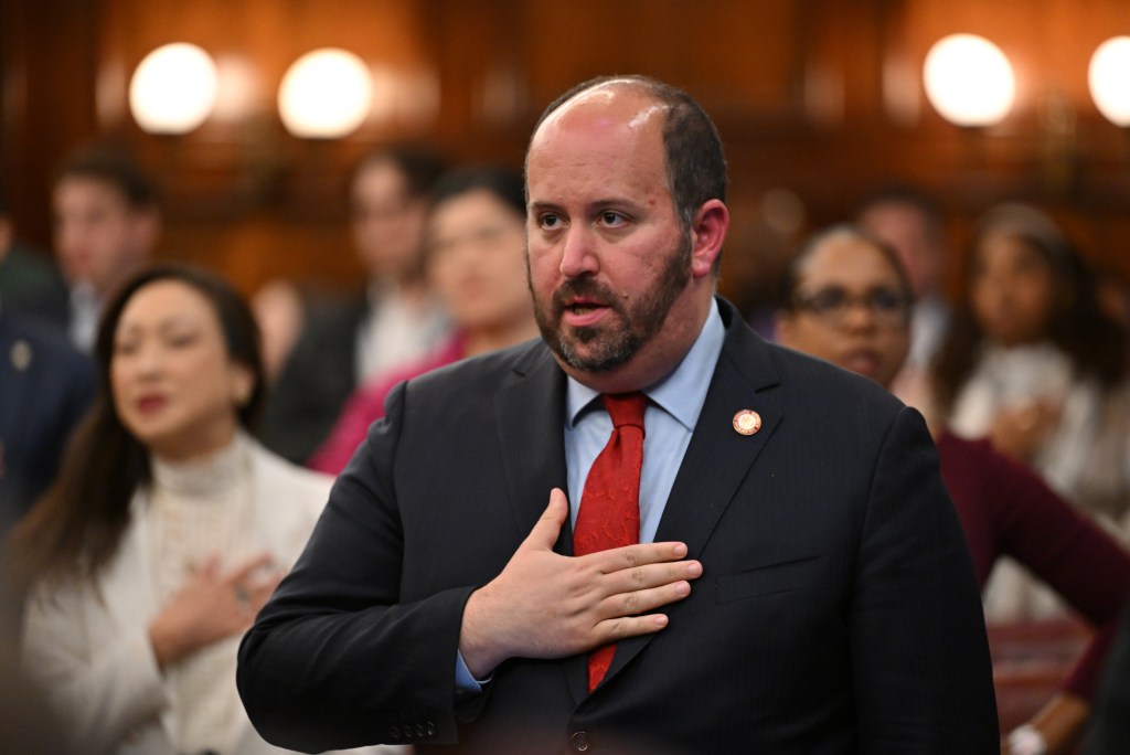 Man in a suit and red tie with his hand over his heart during the NYC FARE ACT vote.