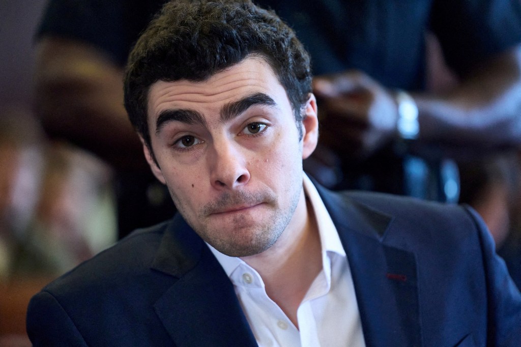 Luigi Mangione in a navy suit and white shirt looks at the camera during a court hearing.