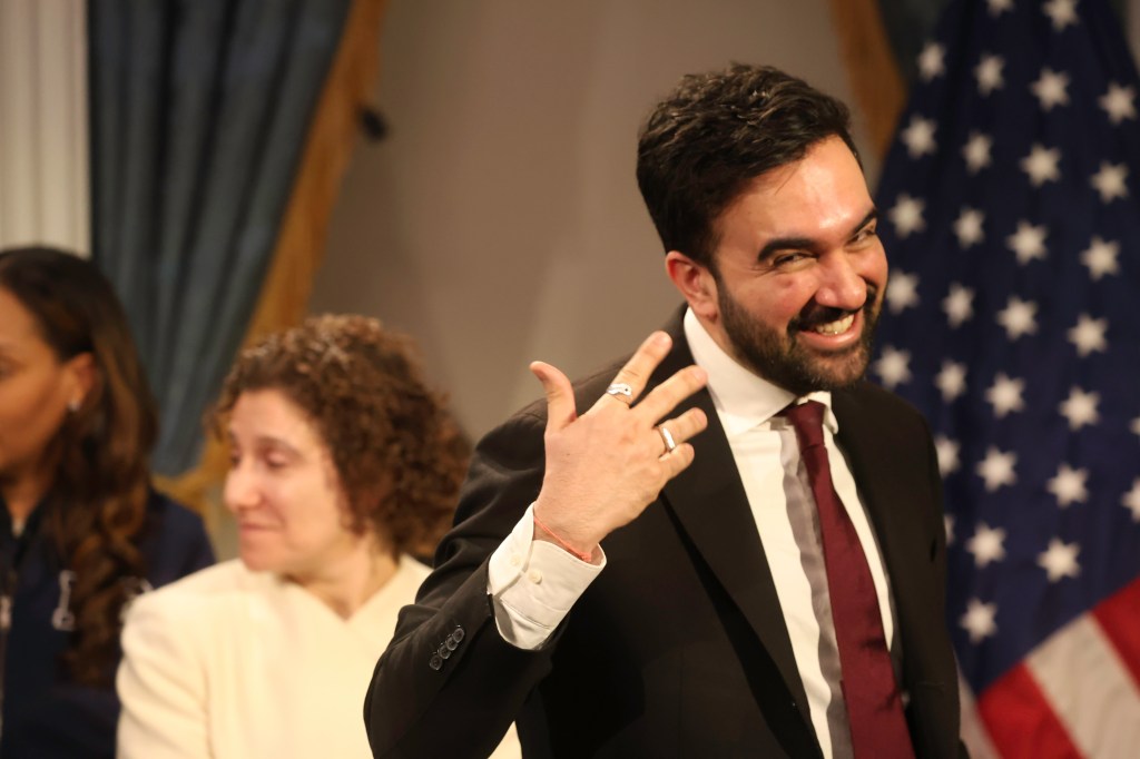 NYC Mayor Zohran Mamdani smiling while addressing the media at City Hall.