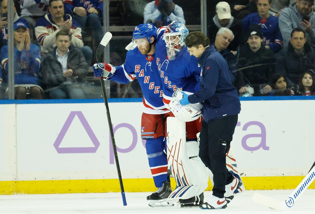 New York Rangers goaltender Igor Shesterkin is helped off the ice by a trainer and New York Rangers defenseman Vladislav Gavrikov.