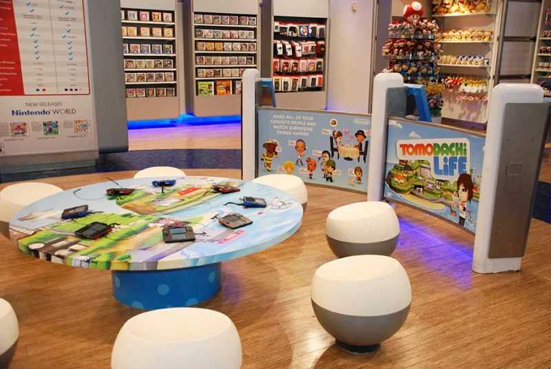 Small mushroom caps chairs and a colorful tale with game consoles on it, inside the Nintendo New York Store