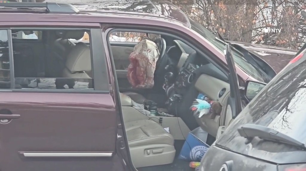 Interior of a car with a bloody airbag deployed from the steering wheel.