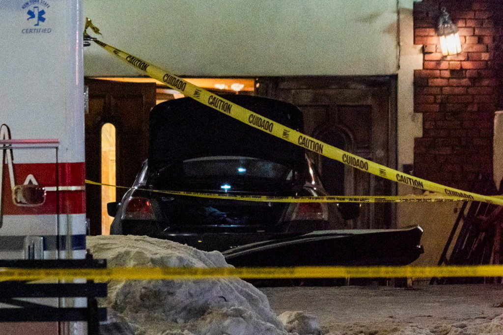 A car with its trunk open is behind police caution tape in front of a building at night.