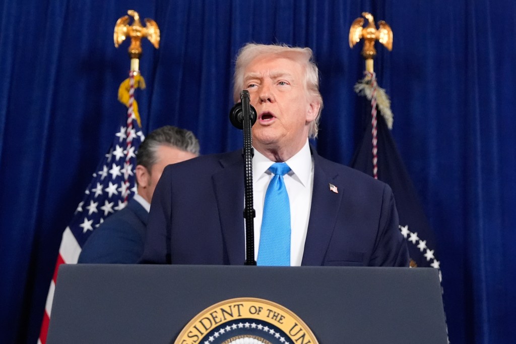 President Donald Trump speaking at a podium with a blue background, flanked by US flags.