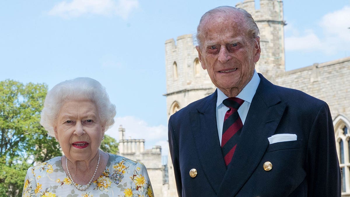 Queen Elizabeth and Prince Philip standing together in front of the castle in formal wear.