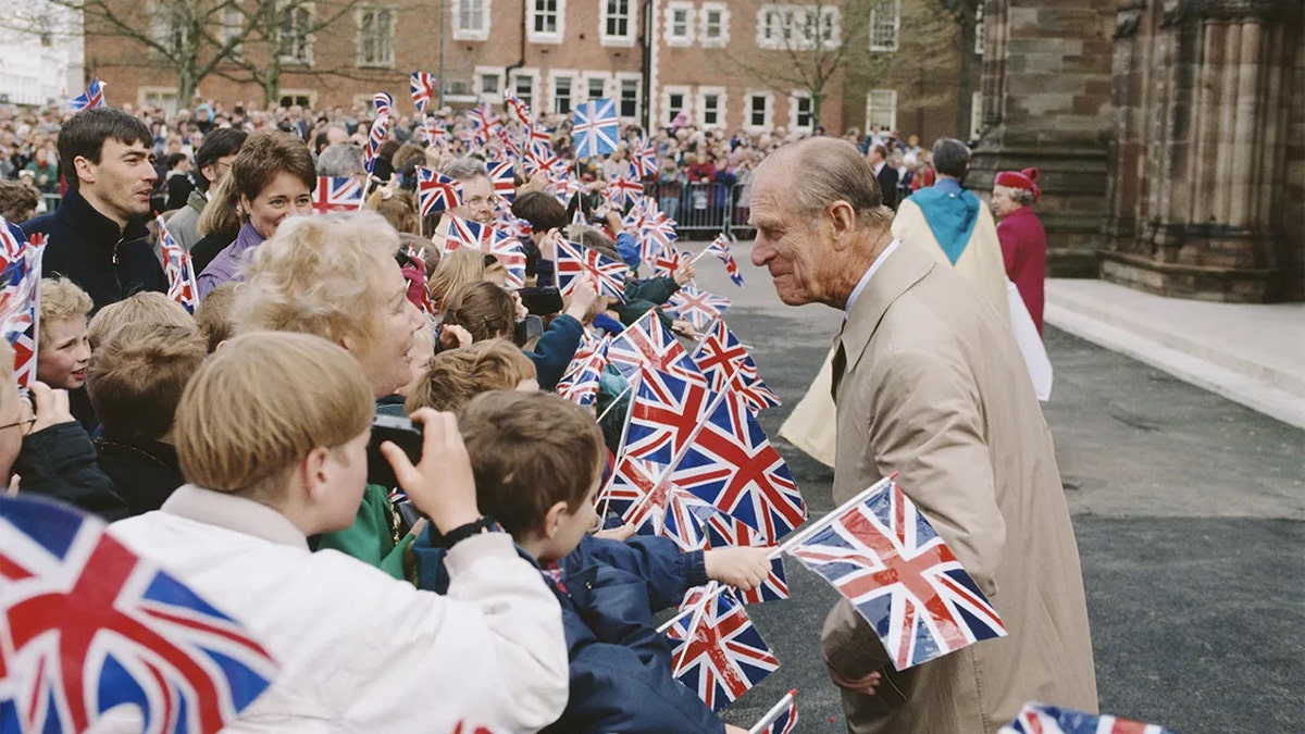 Prince Philip greeting a group of people outside holding the Union Jack flag.