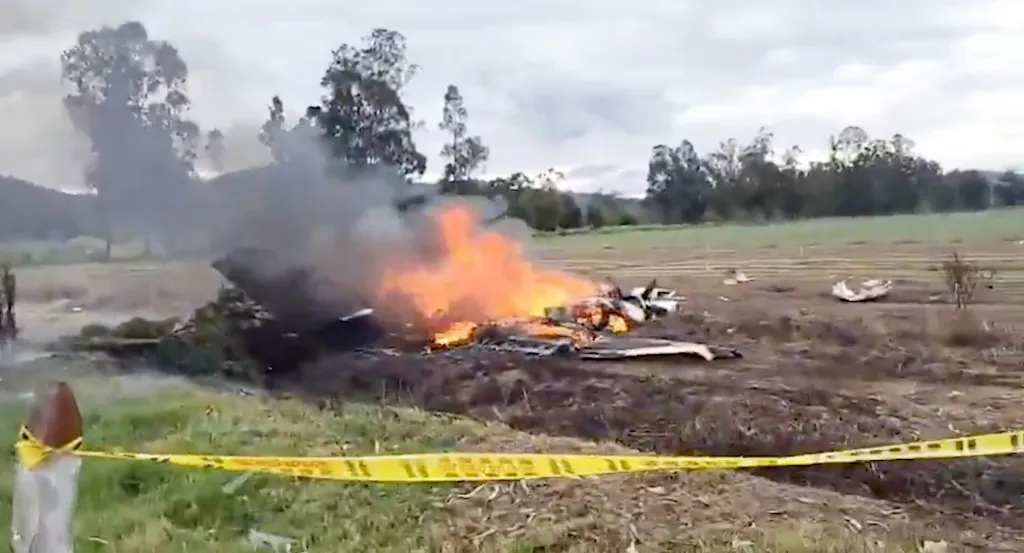 Plane crash site in Paipa, Boyacá with yellow caution tape, smoke, and flames.