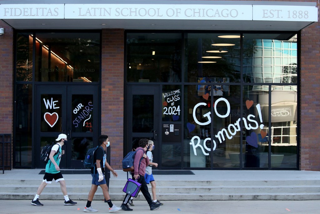 Students wearing face masks walk past the Latin School of Chicago, which has welcoming messages for seniors and the class of 2024 on its windows.