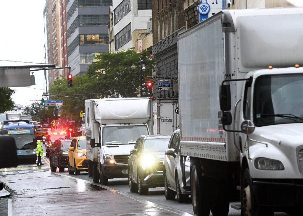 Congested 34th Street in New York, with a bus, trucks, and taxis on a wet road.