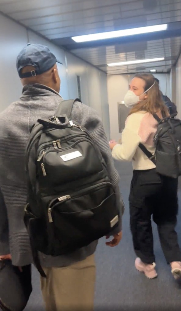 A person wearing a face mask looks back at the person filming as they walk down a jet bridge.