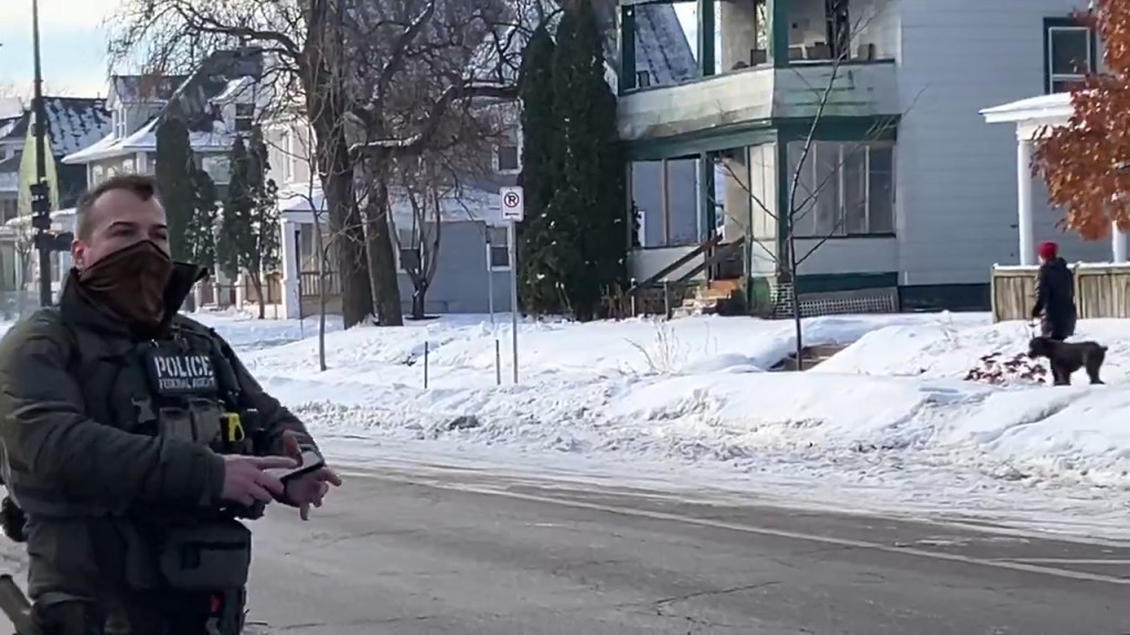 Federal officer in tactical gear with a masked face and a "POLICE FEDERAL AGENT" patch on his chest.