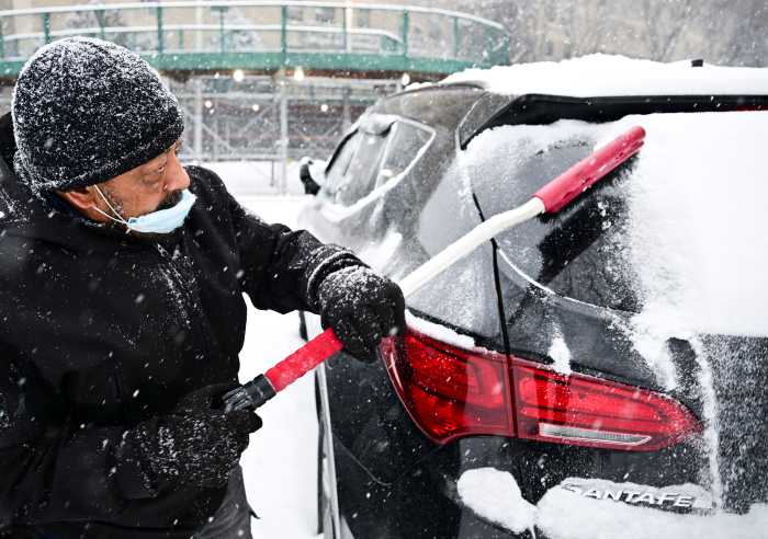 man brushing snow off a car
