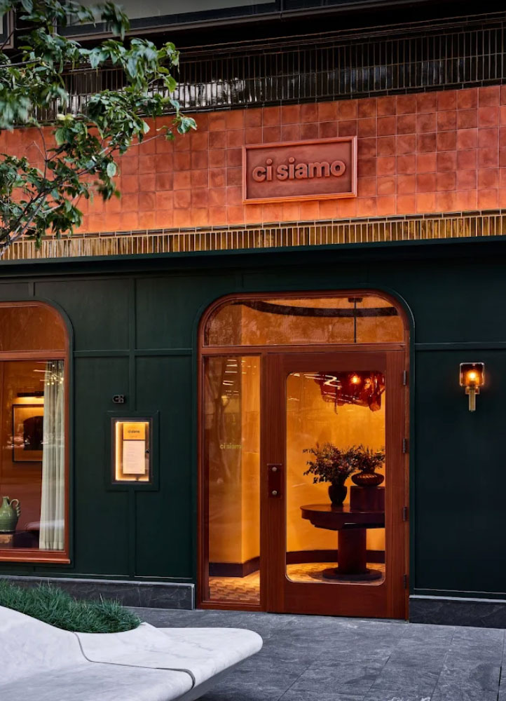 Exterior of Ci Siamo restaurant with a dark green facade and a wooden door.
