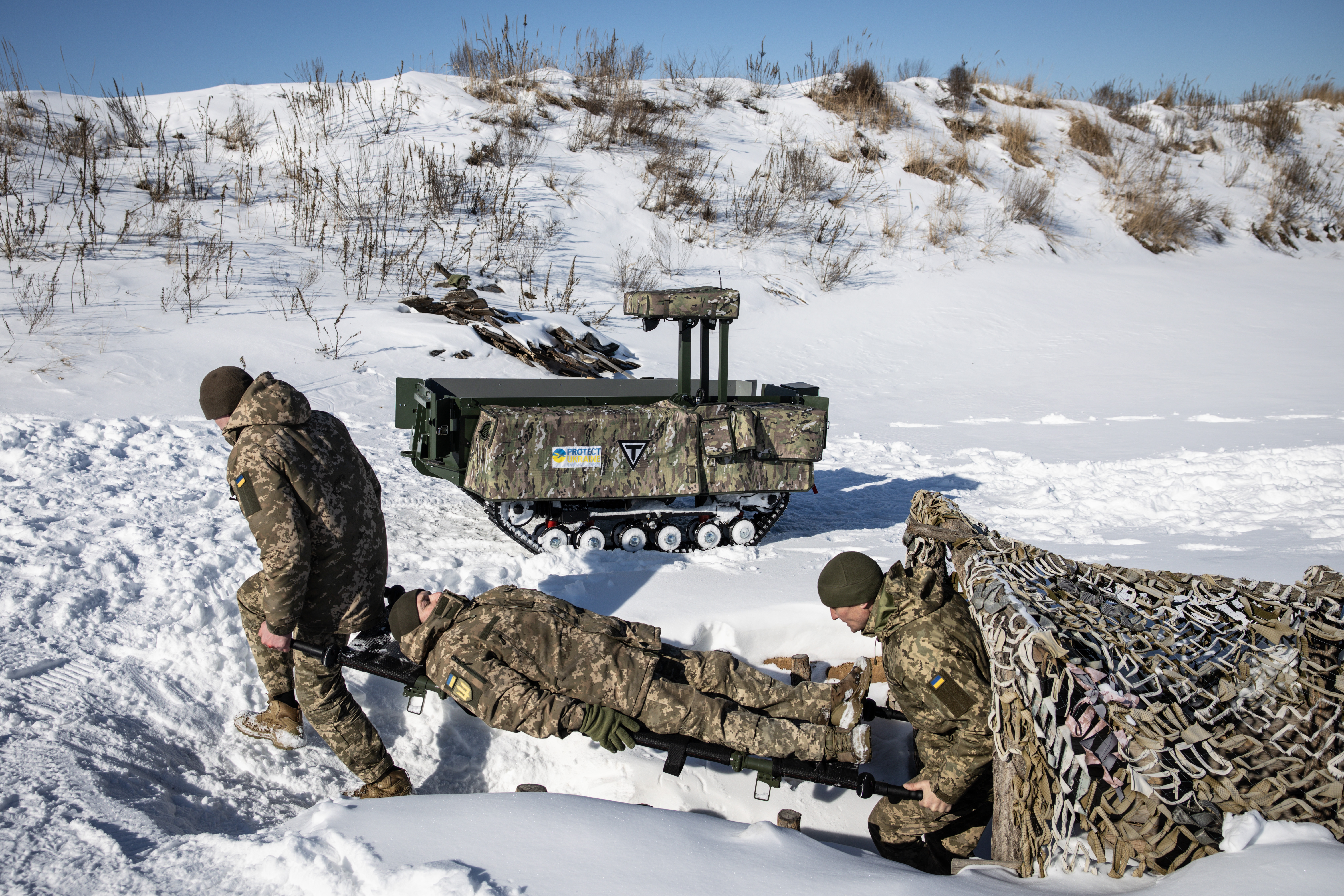 Soldiers demonstrate evacuation procedures using a Tencore Unmanned Ground Vehicle (UGV) TerMIT in a snowy landscape.