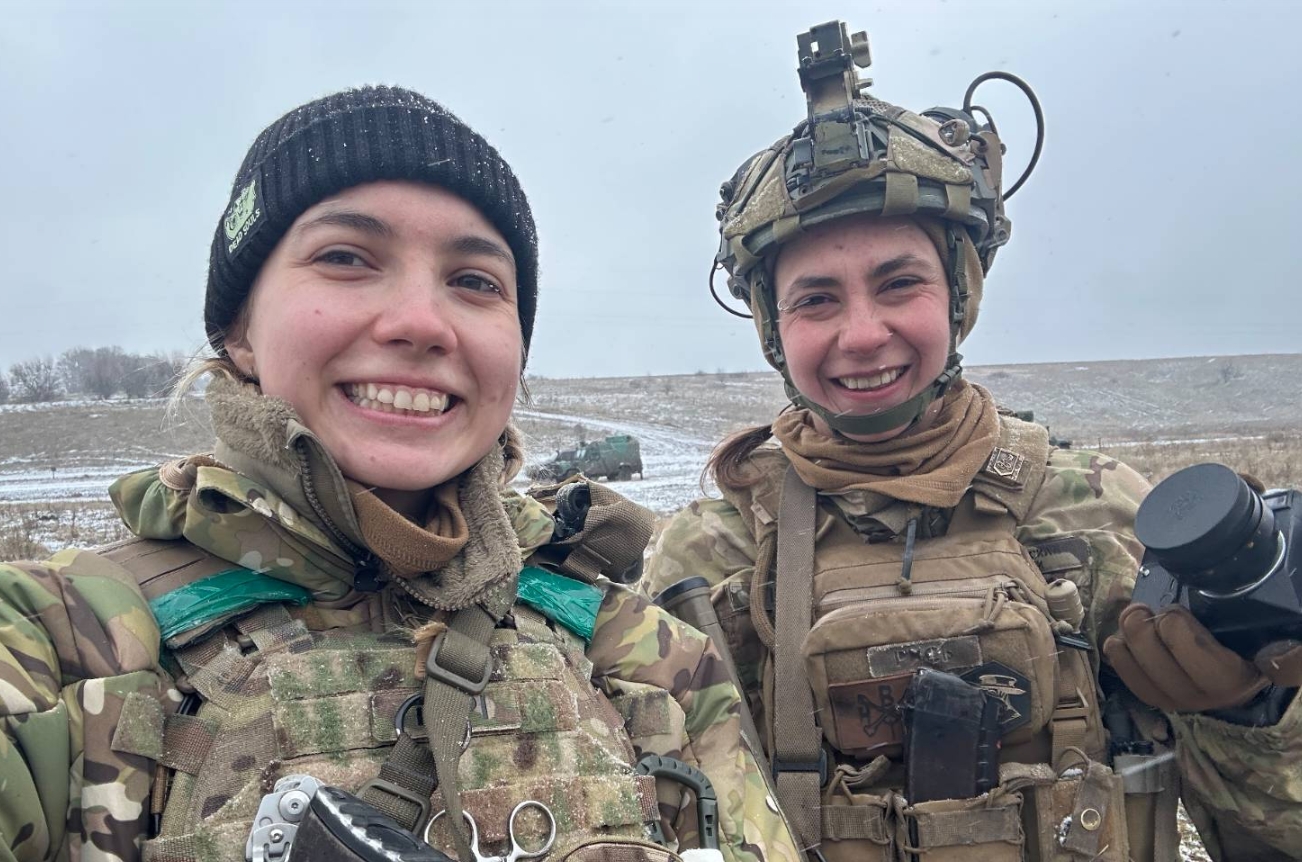 Ukrainian medic Viktoriia Honcharuk (left) and assault trooper Maryna Honcharuk (right) smiling at the camera, wearing military gear and winter clothing in a snowy landscape.