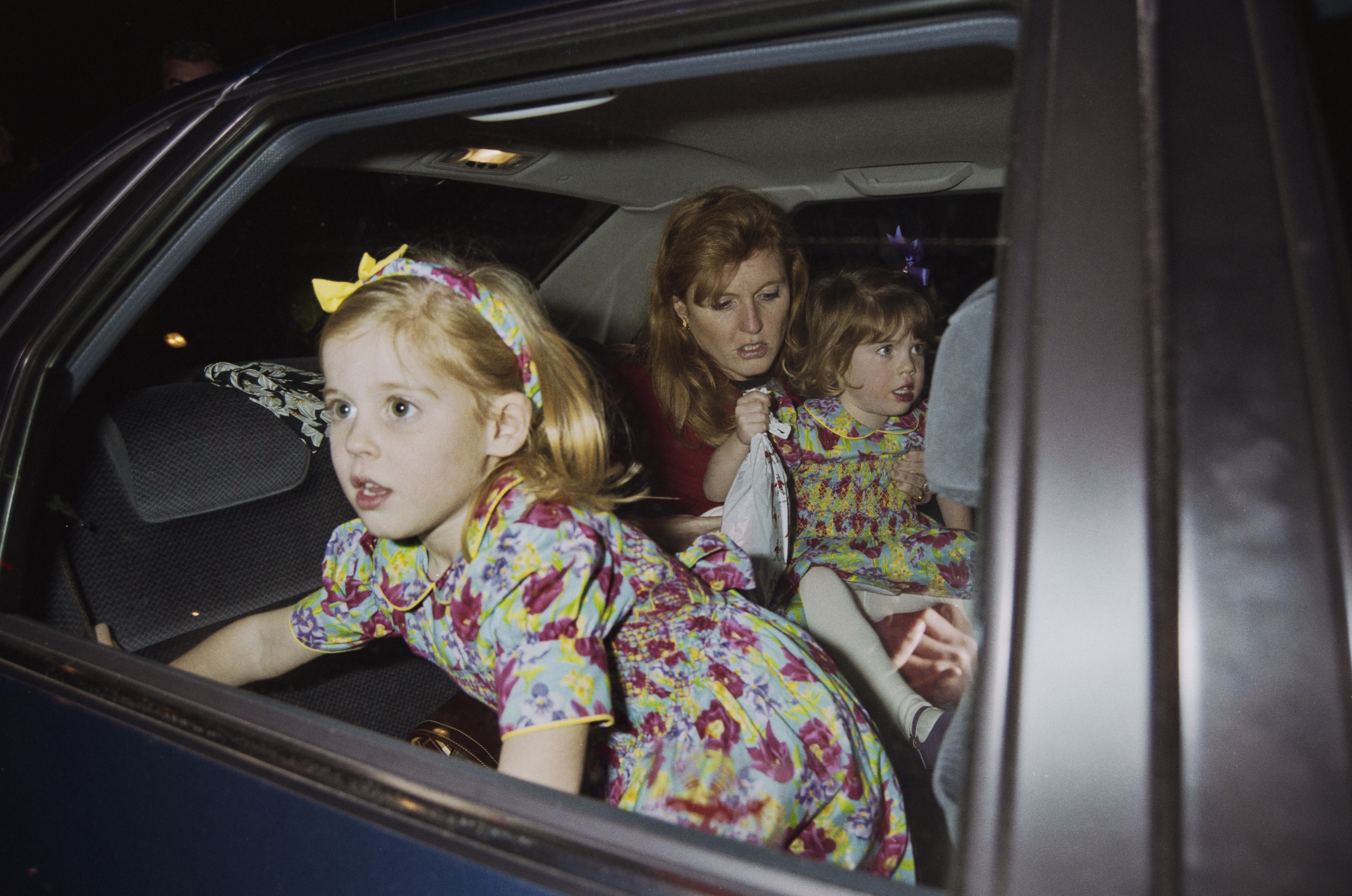 Sarah, Duchess of York with her daughters Princess Eugenie and Princess Beatrice looking out of a car window.