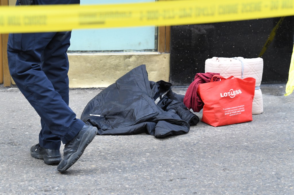 A yellow "CRIME SCENE - DO NOT CROSS" tape hangs above a person's leg, a black jacket, a red Lot-Less shopping bag, and a bundled blanket on the pavement.