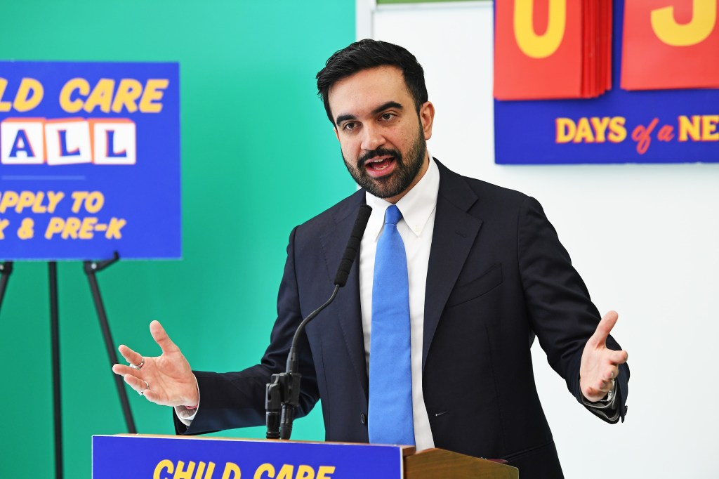 NYC Mayor Zohran Mamdani speaking at a podium with signs about childcare and education.